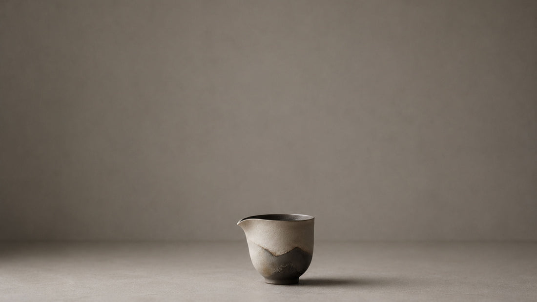 A handmade ceramic pouring vessel, alone on a pale ground.