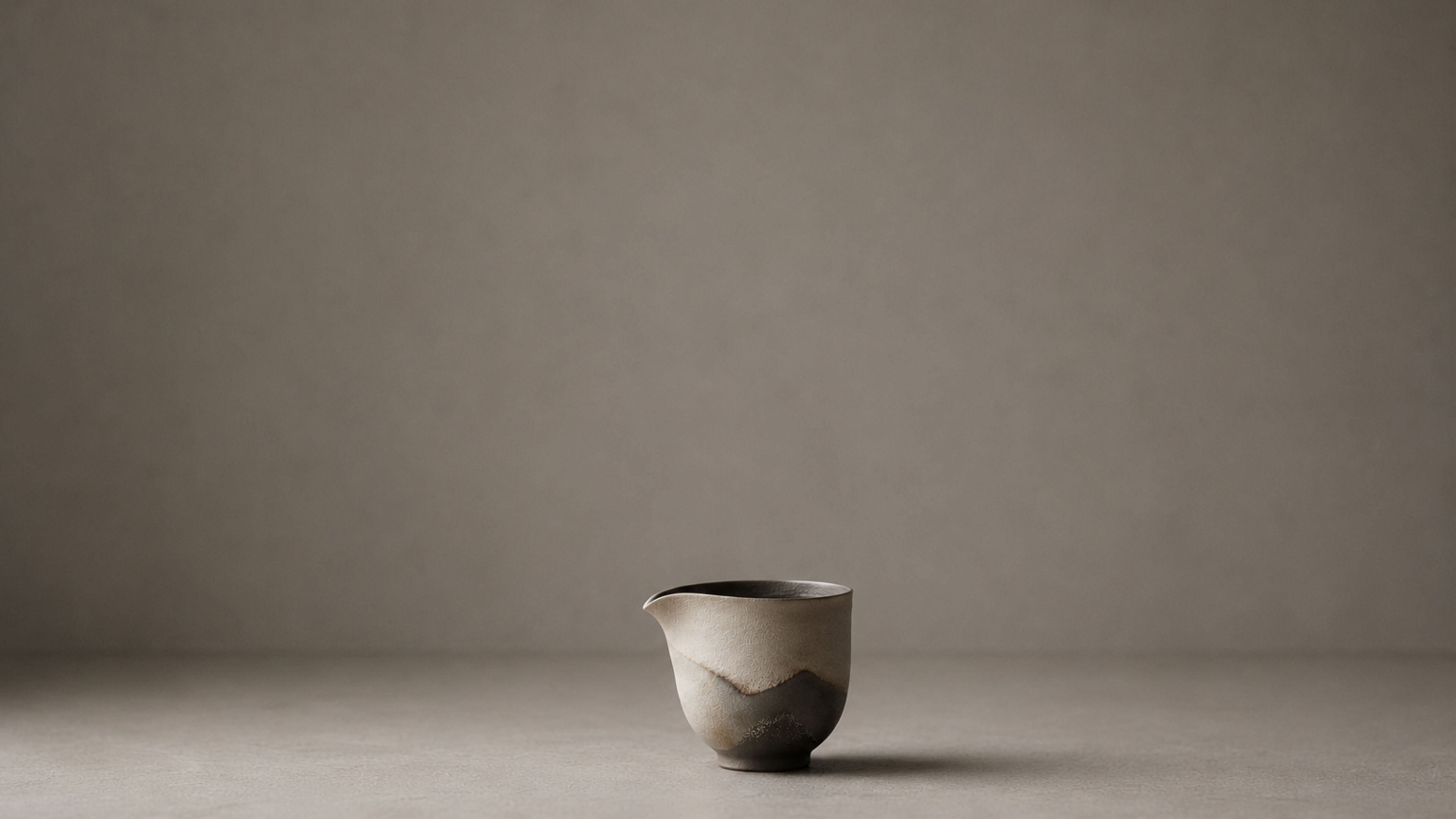 A handmade ceramic pouring vessel, alone on a pale ground.