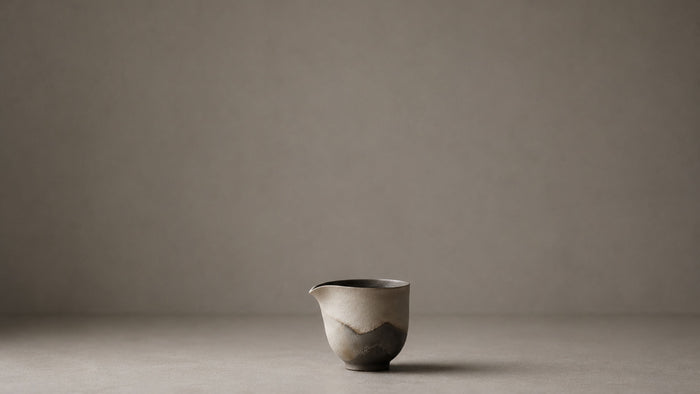 A handmade ceramic pouring vessel, alone on a pale ground.