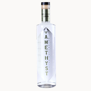 A clear glass bottle of Amethyst botanical spirit with a white geometric label and green lettering, set against a plain off-white background.