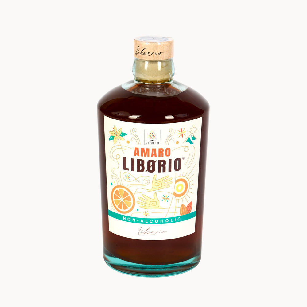 A bottle of Liborio Amaro Liborio non-alcoholic liqueur with amber-brown liquid, a white label with colorful illustrations, and a cork stopper, set against a plain white background.