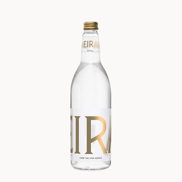 A clear glass bottle of Eira Still water with a gold cap and a white label featuring large gold 'EIR' lettering, set against a plain off-white background.