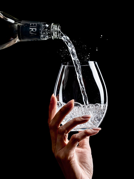 Hand pouring sparkling wine from a bottle into a glass against a black background