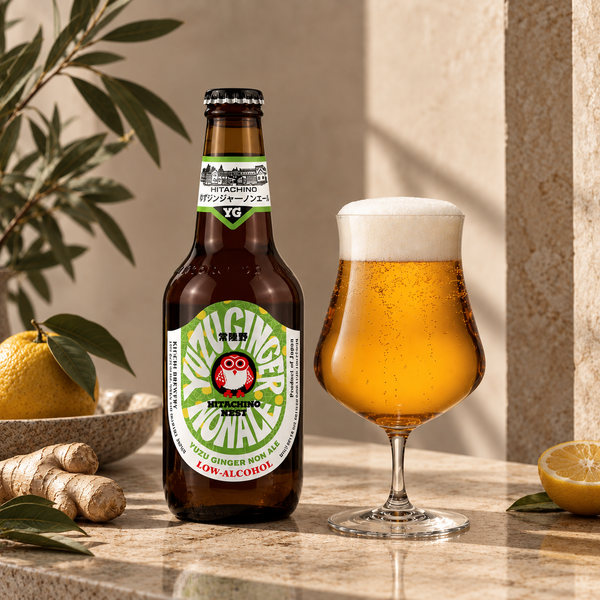 A bottle of Non-Alcoholic Ginger Beer stands next to a filled tulip glass of golden beer with white foam, styled on a stone surface with lemongrass, a lemon, and leaves in a warm indoor setting.