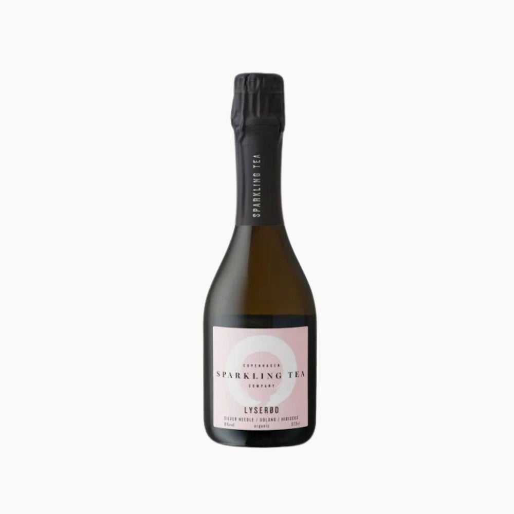 A bottle of Lyserød Copenhagen Sparkling Tea Company sparkling tea, featuring a pale pink label and a black foil-wrapped neck, set against a solid off-white background.