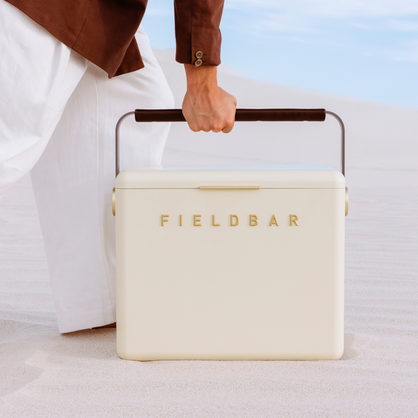 Cream-colored cooler bag with 'FIELDBAR' branding held by a person in a white shirt and brown jacket.
