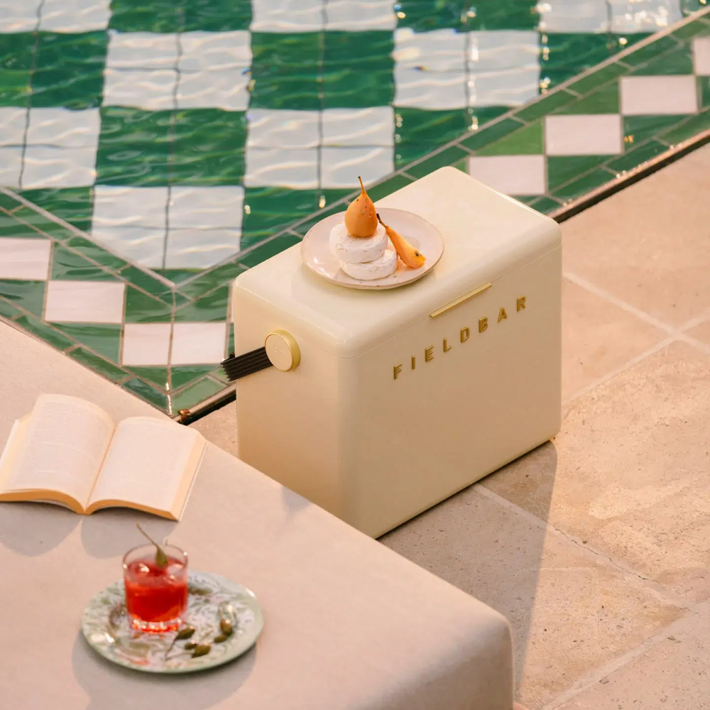 Gin Trunk with 'FIELDBAR' branding next to an open book and a drink on a checkered floor.