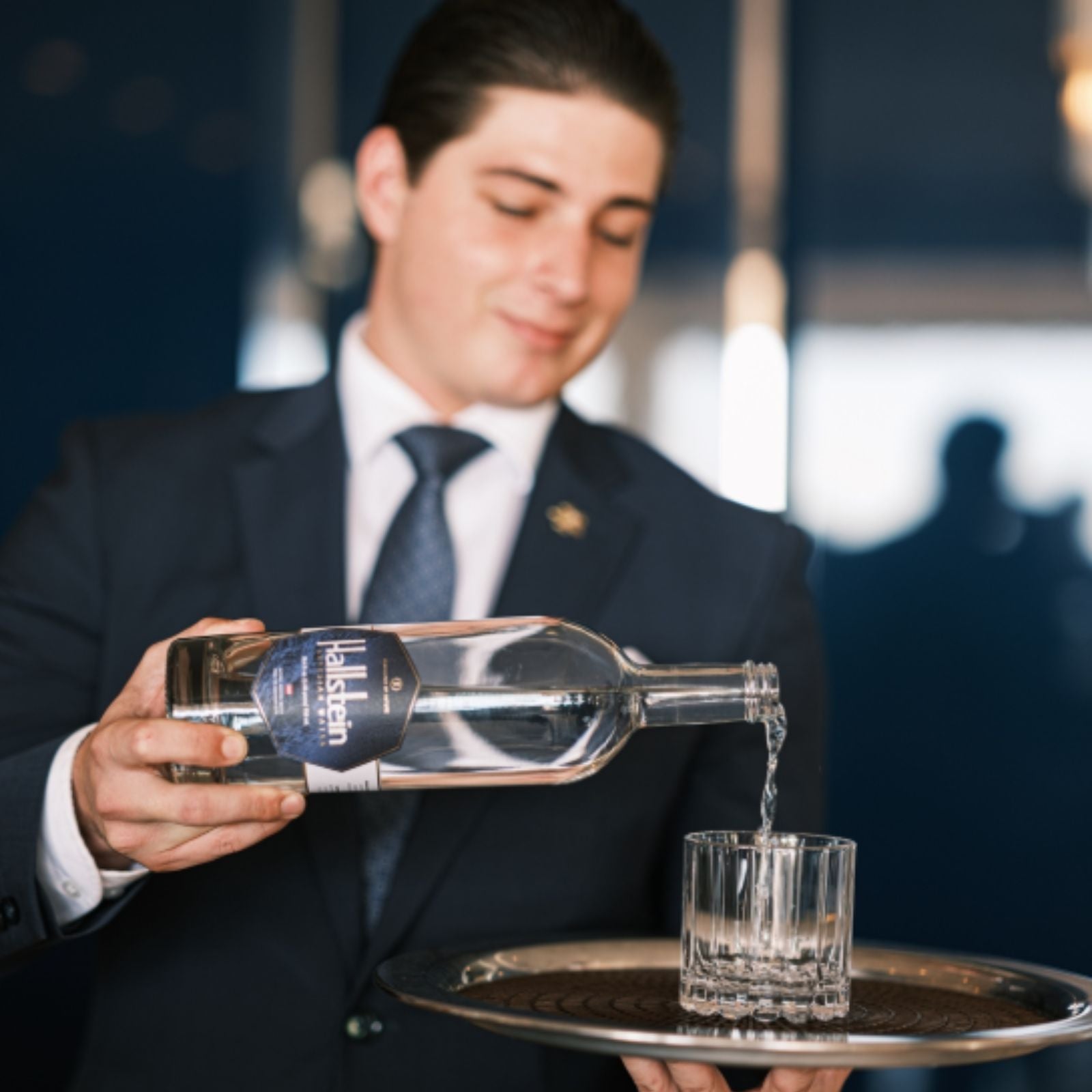 Waiter pouring water from a bottle into a glass on a tray.