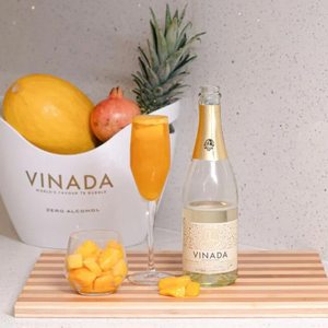 Rienne_Vinada_Bottle and glass of Vinada zero-alcohol sparkling wine with fruit on a wooden board.