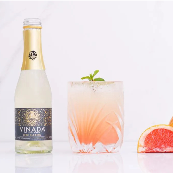 Rienne_Bottle of VINADA non-alcoholic beverage with a glass of a pink drink and a slice of grapefruit on a white background