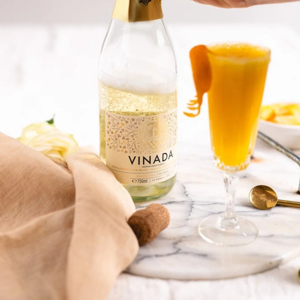 Rienne_Bottle of Vinada sparkling wine with a glass of orange juice on a marble surface.