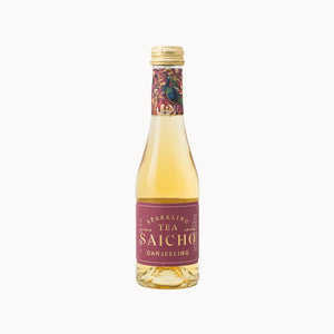 A bottle of Saicho Darjeeling Sparkling Tea, featuring a pale yellow liquid inside a clear glass bottle with a blue label and a decorative cranes pattern on the neck seal, set against a solid off-white background.