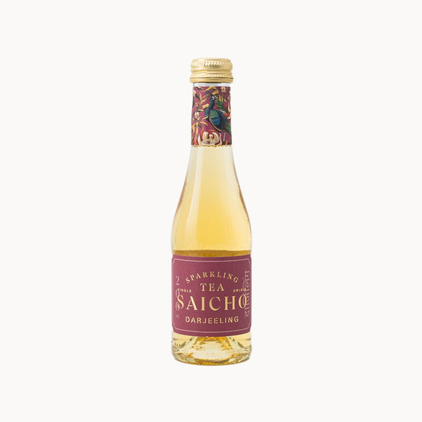 A bottle of Saicho Darjeeling Sparkling Tea, featuring a pale yellow liquid inside a clear glass bottle with a blue label and a decorative cranes pattern on the neck seal, set against a solid off-white background.