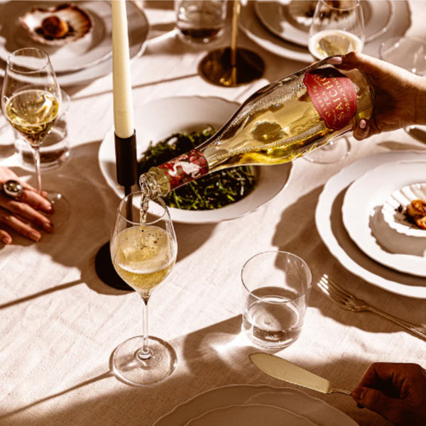 Person pouring champagne into a glass on a dining table with plates and cutlery.