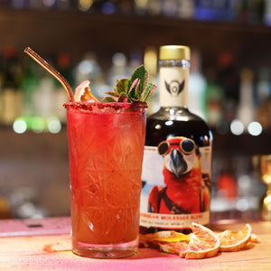 RIENNE Volante Rum bottle on a bar with a tall red zero-proof cocktail, mint and grapefruit garnish