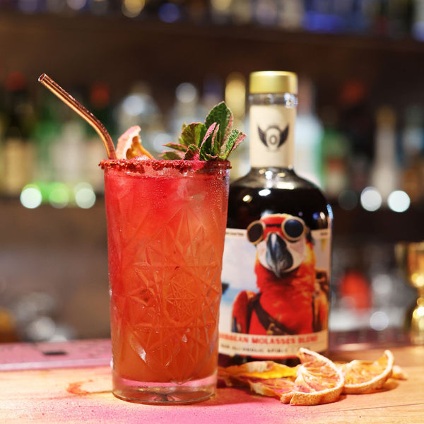 RIENNE Volante Rum bottle on a bar with a tall red zero-proof cocktail, mint and grapefruit garnish